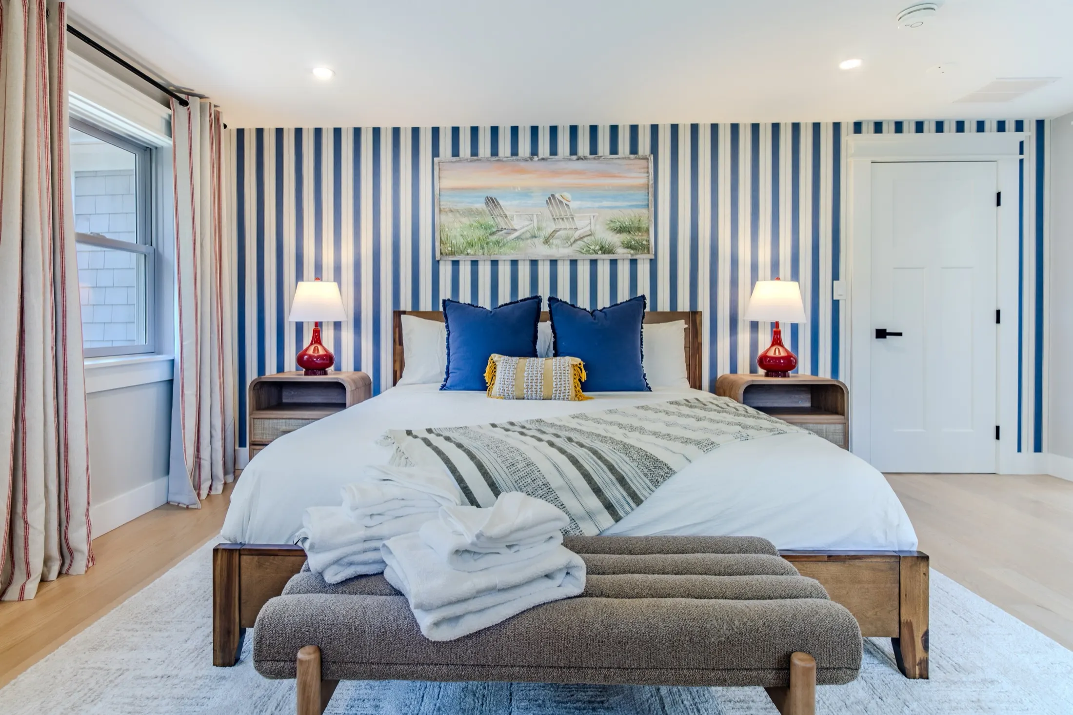 King bedroom with a wooden bed, layered white linens, and a large window.