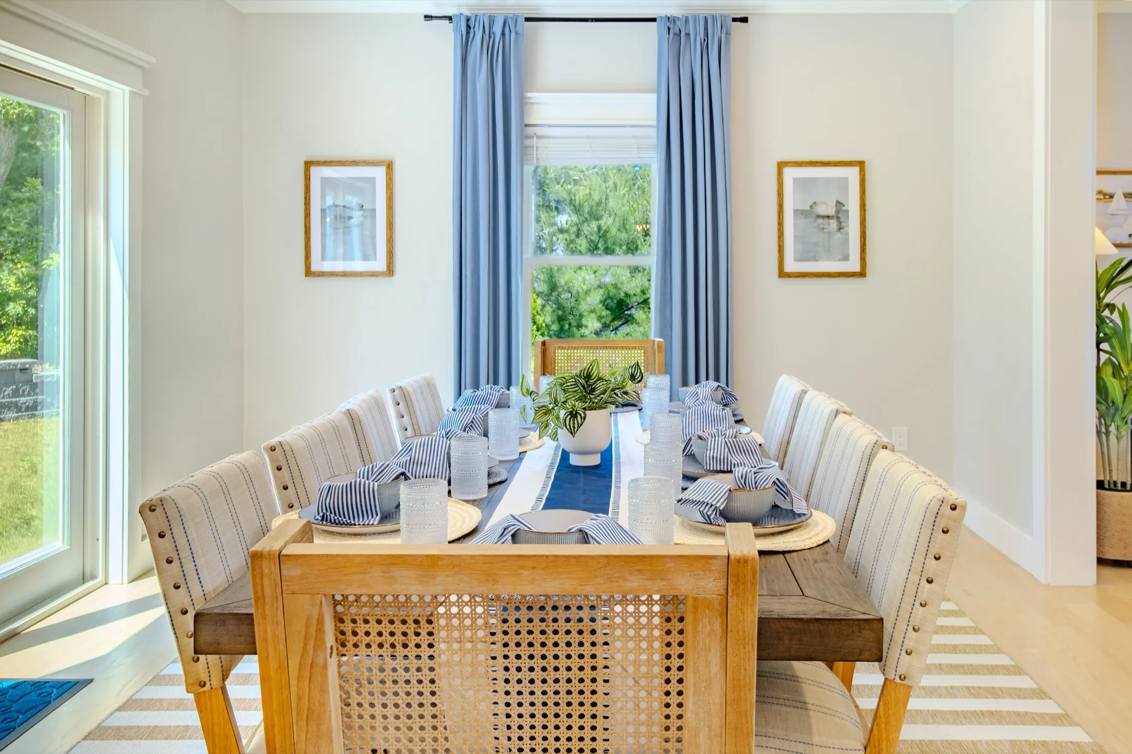 Dining room with a long table, woven chairs, and blue curtains.
