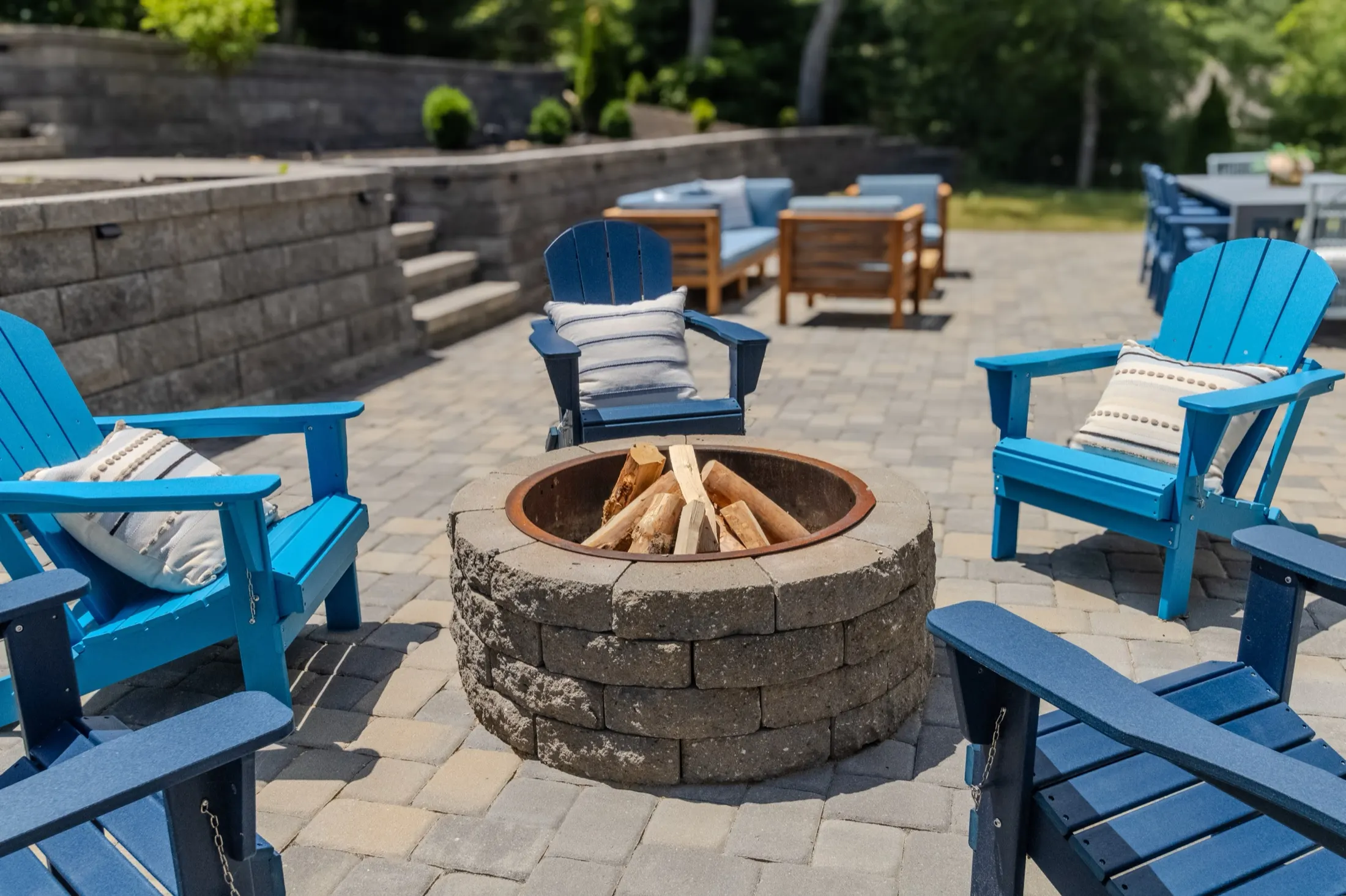 Stone fire pit surrounded by Adirondack chairs at the edge of the woods.