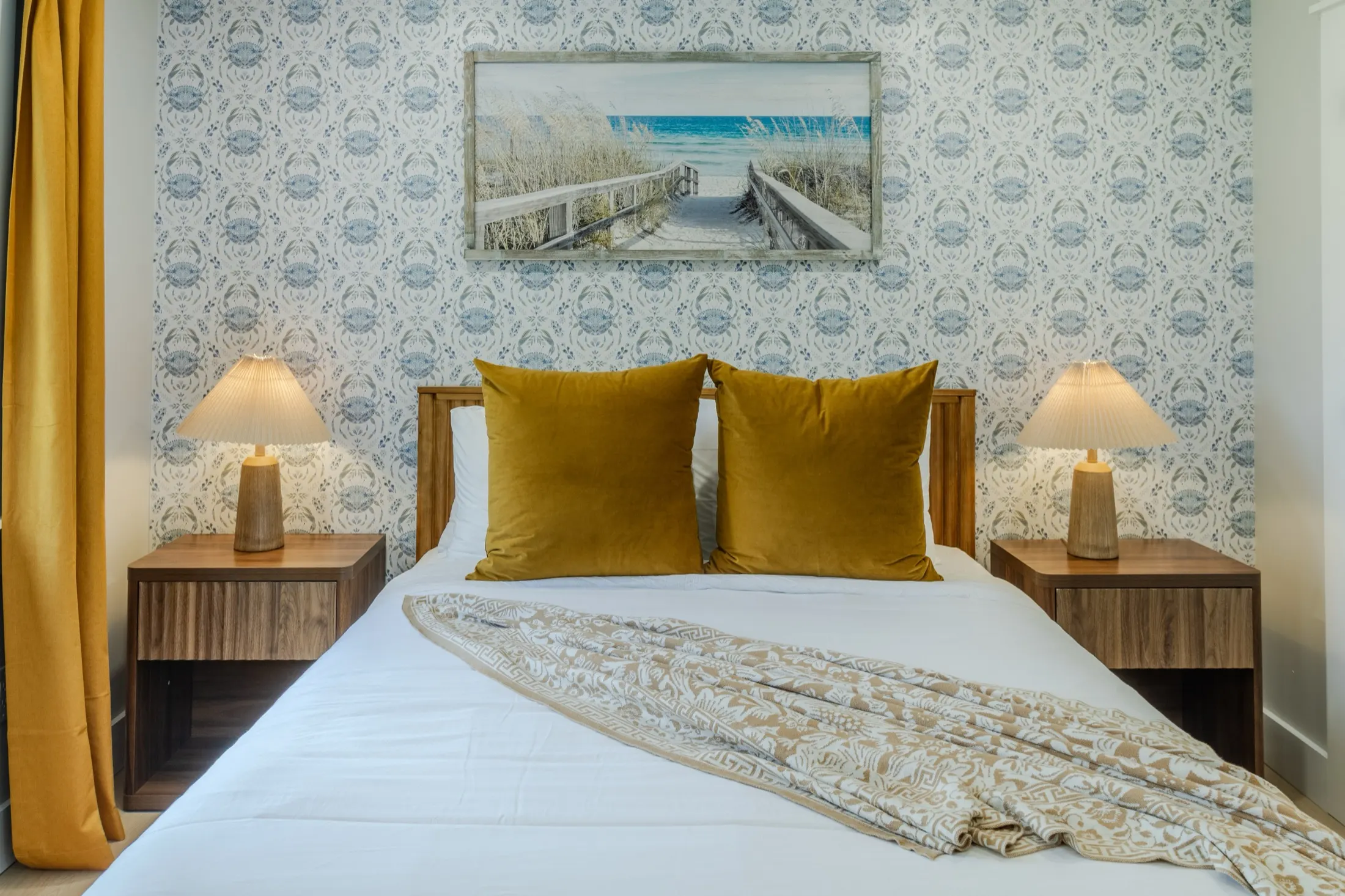 Queen bedroom with bold blue and white striped wallpaper, red lamps, navy pillows, and a coastal painting above the bed.