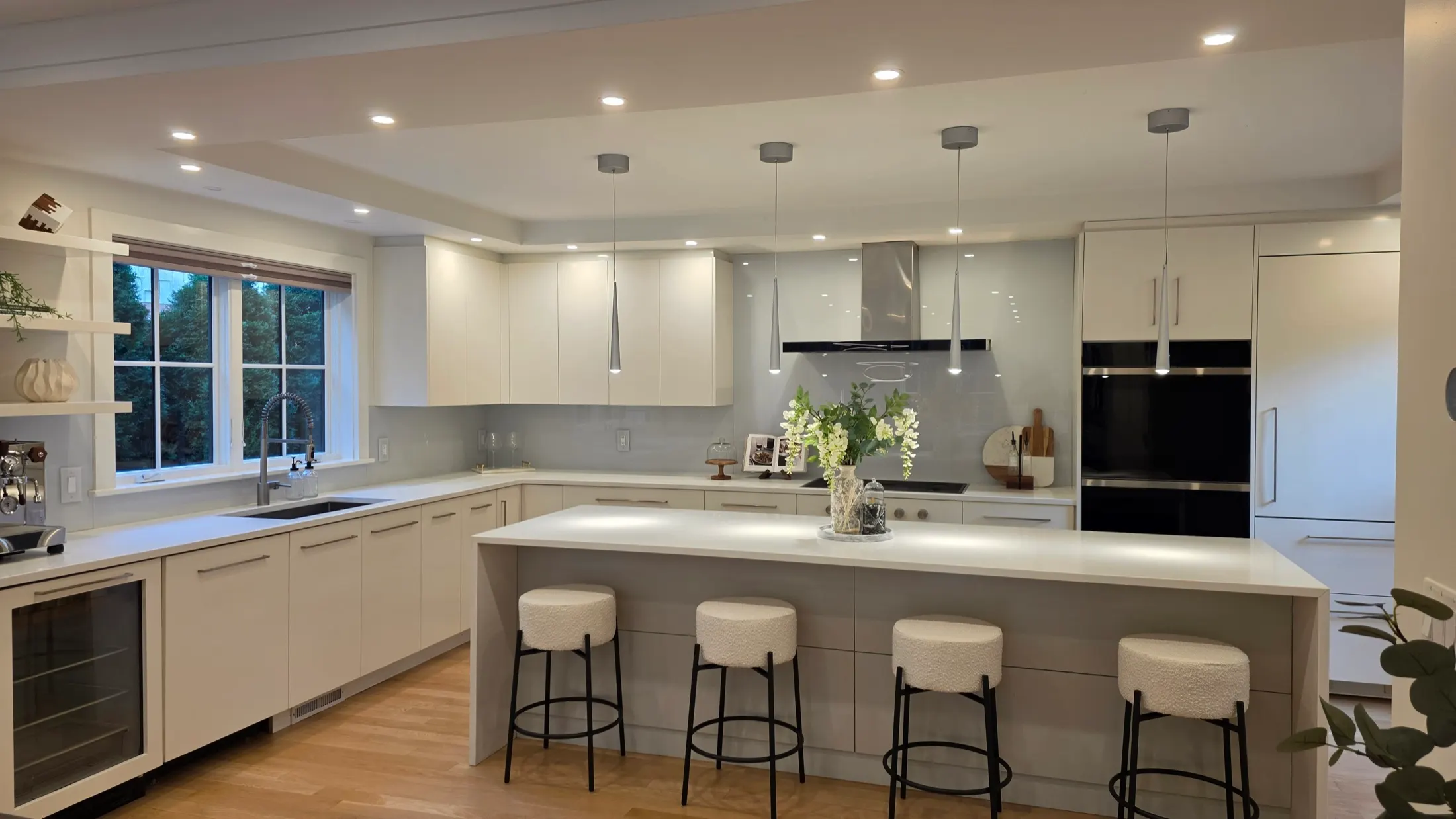 Kitchen with white cabinetry, a waterfall island, four boucle counter stools, and pendant lights, styled with white orchids.
